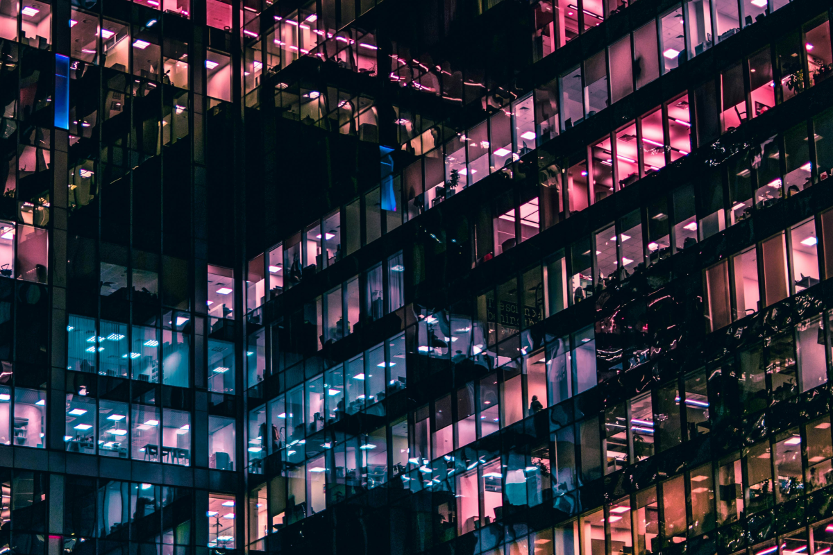 The side of a modern office building with various coloured lights coming from the windows