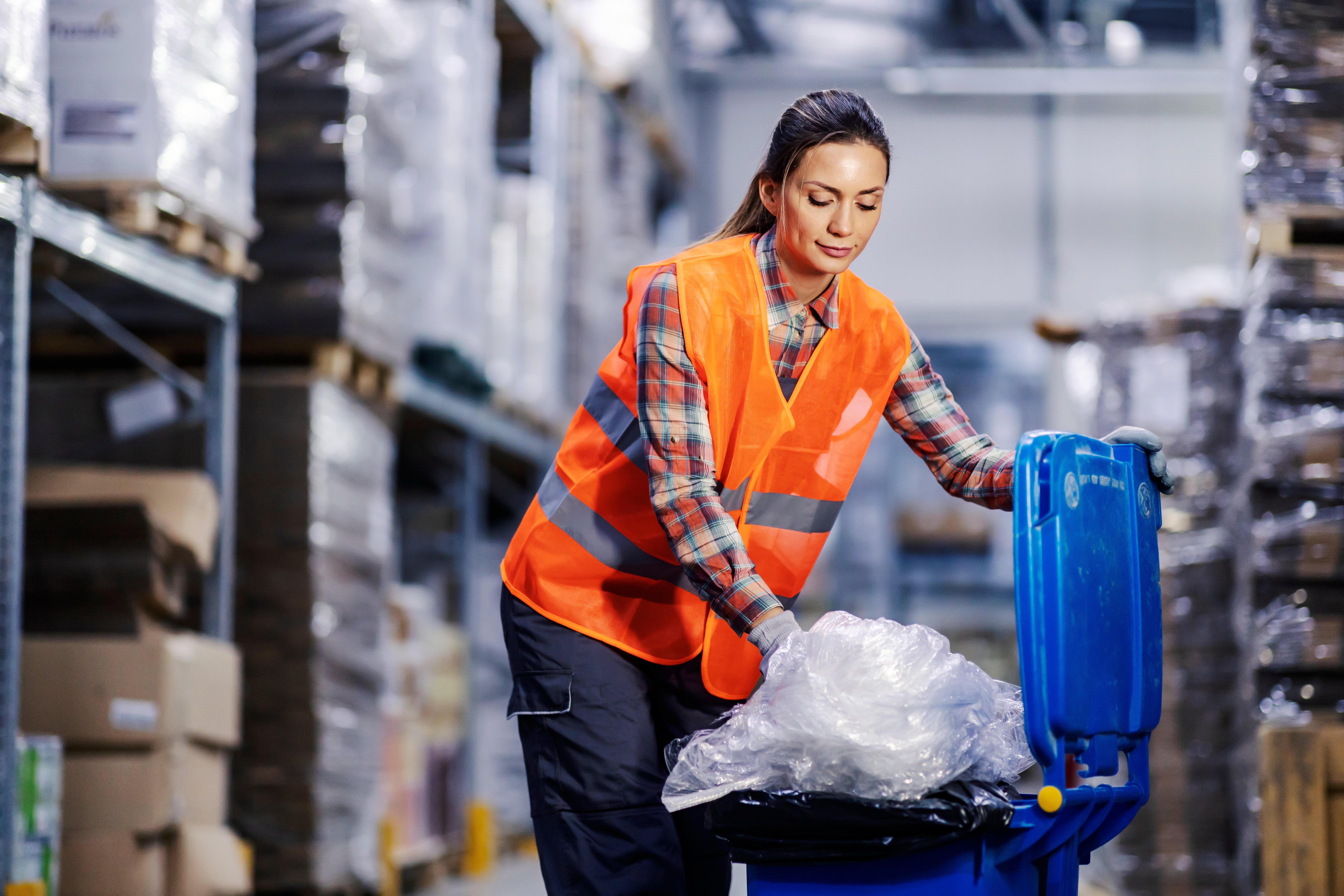 A female storage worker putting plastic bags into recycle bin.